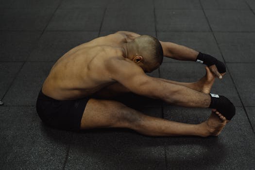 A fit man stretches on a gym floor, emphasizing fitness and flexibility.