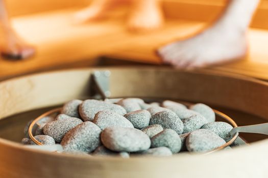 Close-up of sauna stones with blurred feet in a warm, indoor sauna setting.