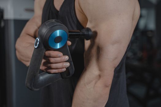 Close-up of a man using a massage gun for muscle relaxation on his arm.