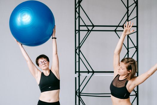 Two women exercising indoors with a blue stability ball, focused on fitness and wellness.