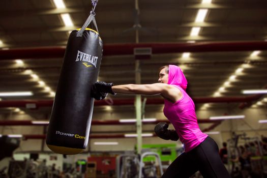 Athletic woman in pink activewear training with a punching bag at an indoor gym for fitness and exercise.