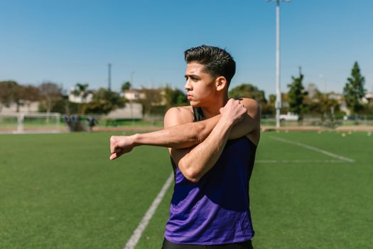 Asian man in sportswear stretching on a sunny field.