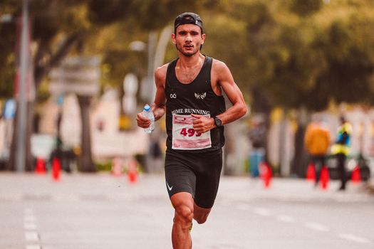 Focused male athlete running a marathon with water bottle on city road