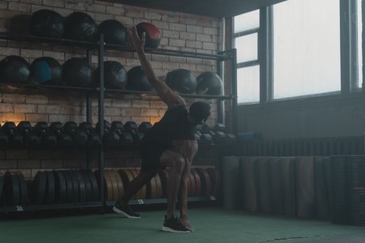 A man performing dynamic stretching exercises in a gym setting with fitness equipment in the background.